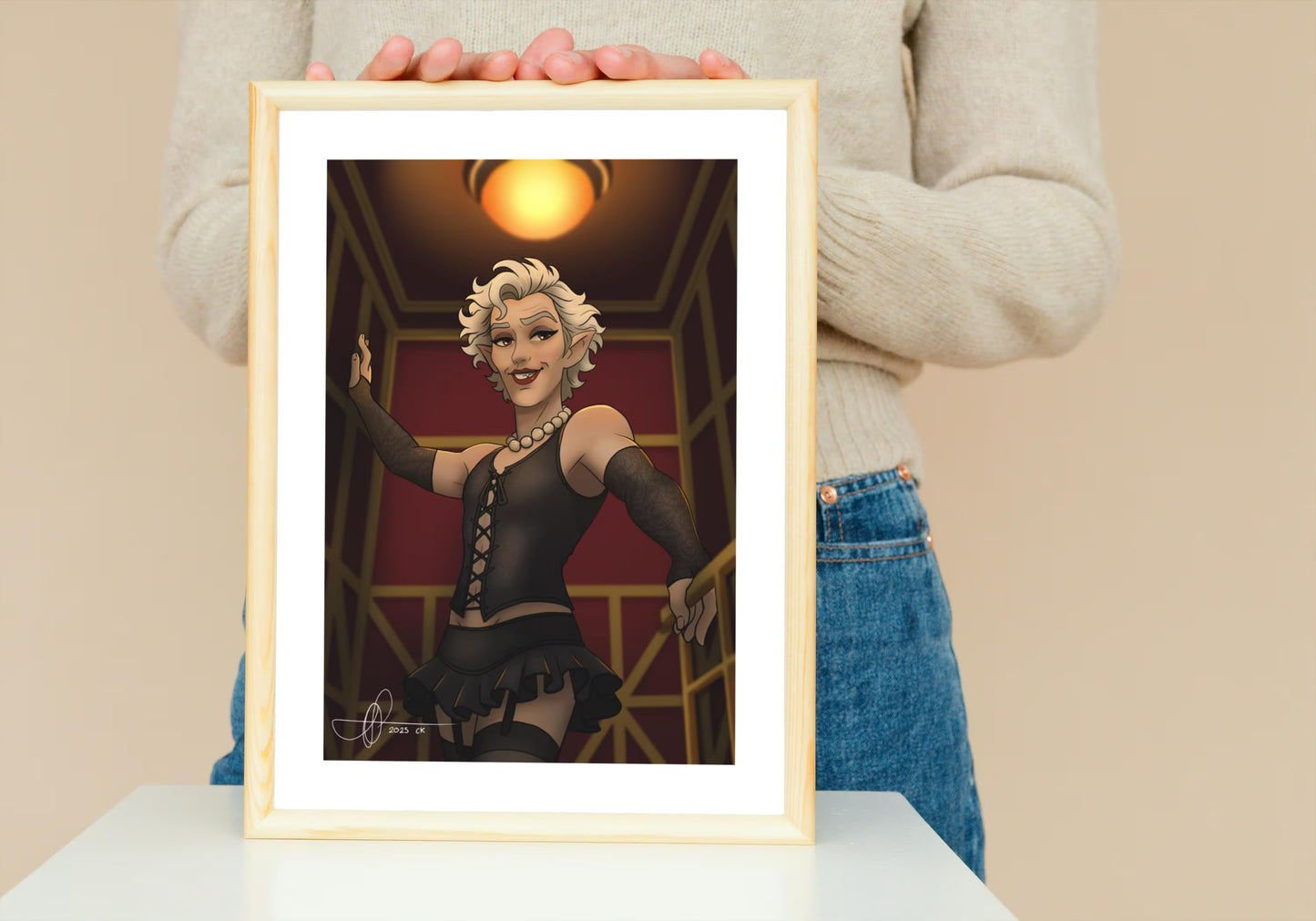 Framed artwork of a stylized character held by a person against a beige background